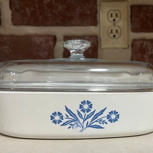 Puede incluir: Plato para hornear blanco con un diseño floral azul y una tapa de vidrio transparente. El plato tiene una forma redondeada y un acabado blanco liso.