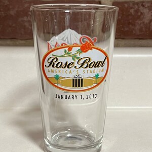 Könnte beinhalten: Ein klares Glas-Pintglas mit einem goldenen und roten Logo, auf dem "Rose Bowl America's Stadium" und "January 1, 2013" steht.