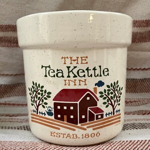 Puede incluir: Jarr&oacute;n de cer&aacute;mica blanco con una ilustraci&oacute;n marr&oacute;n y roja de una casa con techo rojo y chimenea. El texto "THE Tea Kettle INN ESTAB. 1800" est&aacute; impreso en el jarr&oacute;n.