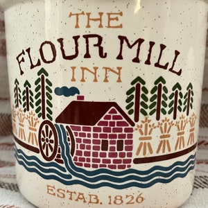 Puede incluir: Jarra de cer&aacute;mica blanca con una ilustraci&oacute;n marr&oacute;n, roja y verde de un molino de harina con el texto "The Flour Mill Inn Estab. 1826".