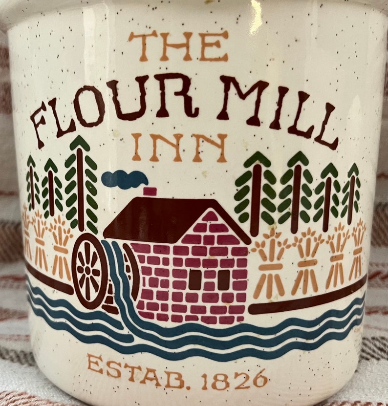 Puede incluir: Jarra de cer&aacute;mica blanca con una ilustraci&oacute;n marr&oacute;n, roja y verde de un molino de harina con el texto "The Flour Mill Inn Estab. 1826".