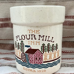 Puede incluir: Jarr&oacute;n de cer&aacute;mica blanca con una ilustraci&oacute;n marr&oacute;n, roja y verde de un molino de harina con el texto "The Flour Mill Inn Estab. 1826".