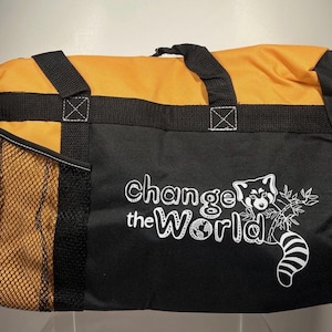 May include: Black and orange duffel bag with the text "Change the World" and a red panda graphic. The bag has a mesh side pocket and black handles. The top of the bag is orange.