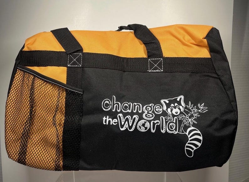 May include: Black and orange duffel bag with the text "Change the World" and a red panda graphic. The bag has a mesh side pocket and black handles. The top of the bag is orange.