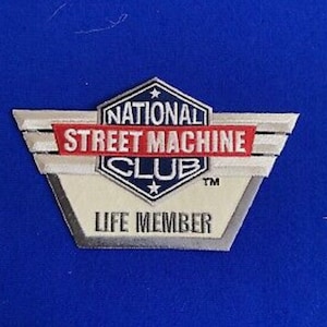 Könnte beinhalten: Ein weißer, silberner und roter Patch mit dem Text "National Street Machine Club" und "Life Member" in einem blauen und weißen sternförmigen Design.