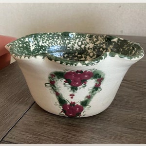May include: A white ceramic bowl with a green and white speckled glaze. The bowl has a scalloped rim and a floral design in green and red.