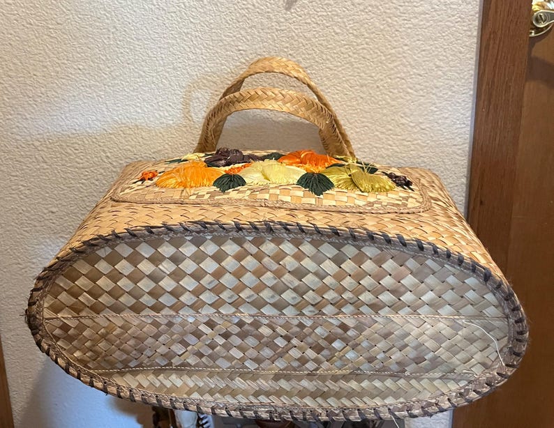 K&ouml;nnte beinhalten: Eine geflochtene Strohtasche mit Blumenmuster. Die Tasche ist aus nat&uuml;rlichen Materialien gefertigt und hat einen einzigartigen Vintage-Stil.
