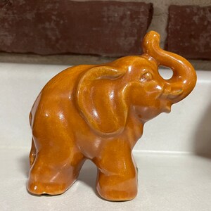 May include: A brown ceramic elephant figurine with a raised trunk. The elephant is standing on all four legs and has a glossy finish.