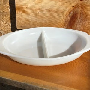 May include: White oval divided serving dish with a center divider. The dish has a smooth, glossy finish.
