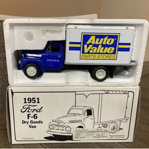 Puede incluir: Un modelo a escala 1/34 de un camión Ford F-6 de 1951 para mercancías secas. El camión está pintado de azul con una cabina blanca y una caja blanca. La caja tiene el logotipo de Auto Value Parts Stores en amarillo y azul. El modelo está en su embalaje original.