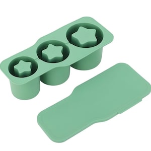May include: A light green silicone ice cube tray with three star-shaped molds and a matching lid. The tray is designed to make star-shaped ice cubes. The word "pup" is printed on each star. The lid is rectangular with rounded edges.