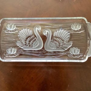 May include: Rectangular glass serving tray with etched swan and water lily design. The tray features two swans facing each other, surrounded by water lilies. The edges have decorative handles.