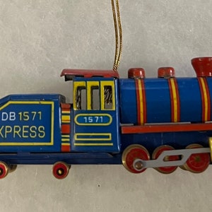 May include: A blue and red toy train engine ornament with a gold string for hanging. The engine has yellow stripes and the text "DB 1571 EXPRESS" on the side.
