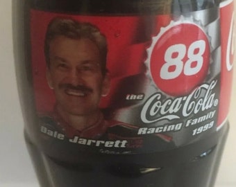 May include: A Coca-Cola bottle featuring Dale Jarrett, a NASCAR driver, with the number 88 and the text "The Coca-Cola Racing Family 1999".