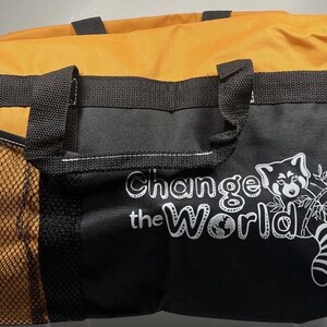 May include: A black and orange duffel bag with black handles and a side mesh pocket. The bag features the text "Change the World" with a red panda graphic.