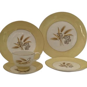 Puede incluir: Juego de vajilla vintage amarillo y blanco con diseño de trigo. El juego incluye una taza y un platillo, junto con platos de varios tamaños. Los platos y la taza tienen un borde dorado.