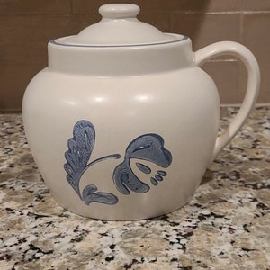 Peut inclure: Casserole en céramique blanche avec un motif floral bleu et un couvercle. La casserole a une poignée sur le côté.