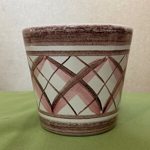 May include: A white ceramic planter with a brown and pink geometric pattern. The planter has a wide, round opening and a slightly tapered body.