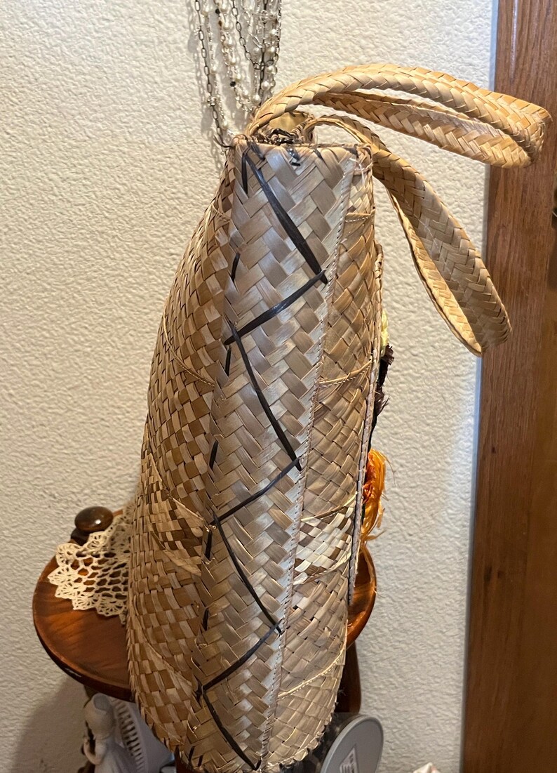 K&ouml;nnte beinhalten: Eine geflochtene Strohtasche mit braunen und schwarzen Akzenten. Die Tasche hat eine gro&szlig;e, rechteckige Form und zwei lange Henkel. Die Tasche ist aus nat&uuml;rlichen Materialien gefertigt und hat einen rustikalen, handgefertigten Look.