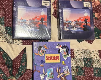 May include: Two purple stamp albums with a space-themed design and a purple album with a cartoon character design. The albums have the text "STAMP ALBUM" and "$9.99" printed on the front.
