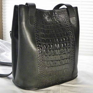 May include: Black leather handbag with a crocodile-textured front panel. The bag has a structured shape with a top handle and a shoulder strap. The bag is made of a smooth leather material and has a sleek, modern design.