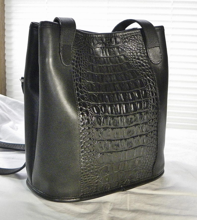 May include: Black leather handbag with a crocodile-textured front panel. The bag has a structured shape with a top handle and a shoulder strap. The bag is made of a smooth leather material and has a sleek, modern design.