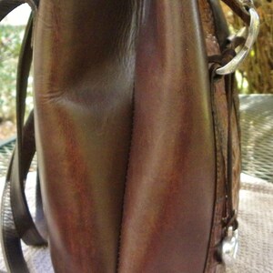 May include: A brown leather shoulder bag with a rectangular shape. The bag has a top handle and a long strap for carrying over the shoulder. The leather appears to be distressed, with variations in color and texture.