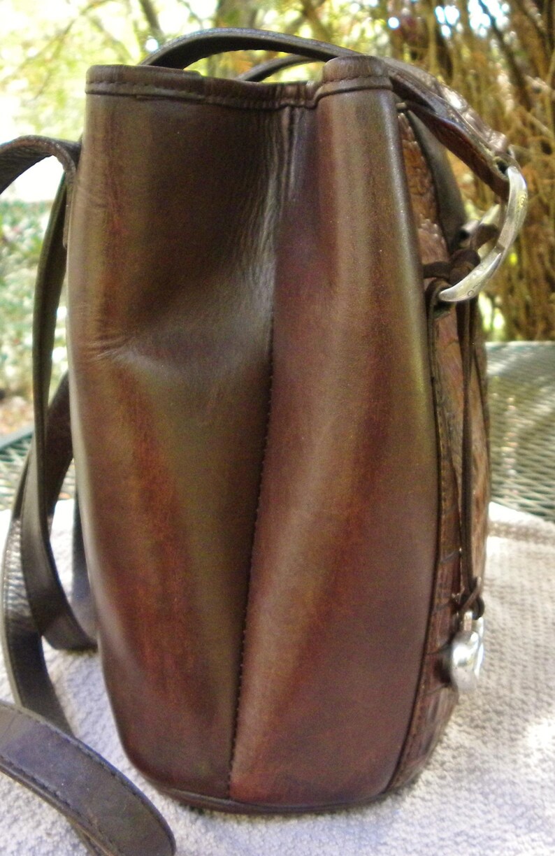 May include: A brown leather shoulder bag with a rectangular shape. The bag has a top handle and a long strap for carrying over the shoulder. The leather appears to be distressed, with variations in color and texture.