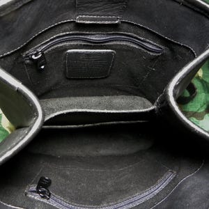 May include: Black leather handbag with multiple interior compartments and a zippered closure. The bag features a rectangular shape with a top flap and a shoulder strap. The interior includes a small leather tag.