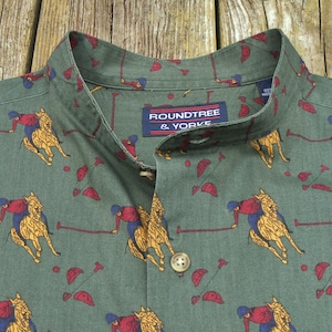 May include: Green button-up shirt with a polo-themed pattern. The design features riders on horseback in yellow and red, with polo mallets and helmets. The shirt has a mandarin collar and the brand name "ROUNDTREE & YORKE" is visible.