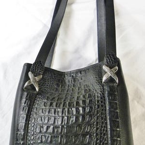 May include: Black leather tote bag with a crocodile-textured center panel. The bag features two shoulder straps and silver-colored decorative accents. The bag is designed with a structured shape and a classic, elegant style.