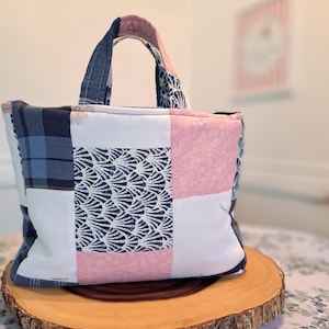Può includere: Una borsa tote patchwork caratterizzata da una combinazione di quadrati di tessuto a quadri blu navy, bianco tinta unita, un motivo a conchiglie a ventaglio blu navy e bianco e una stampa floreale rosa chiaro. Include due manici in tessuto abbinati.