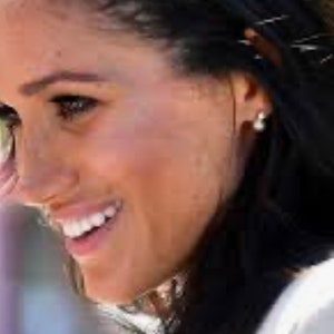 Può includere: Una donna con lunghi capelli scuri sorride con la testa inclinata di lato. Indossa una camicia bianca e ha un piccolo orecchino all'orecchio sinistro.