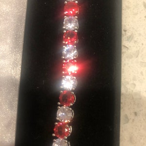 May include: A silver bracelet with alternating red and clear round stones.