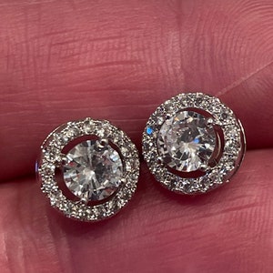 May include: A pair of silver earrings with a round, clear crystal center surrounded by a halo of smaller crystals.