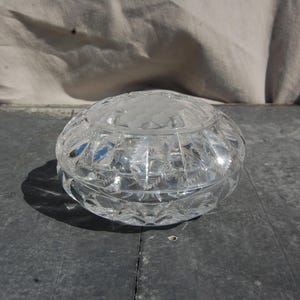 May include: A clear glass trinket box with a cut glass design. The box is round and has a lid.