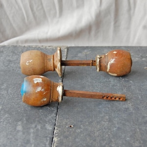 Może przedstawiać: Dwa antyczne drewniane uchwyty do drzwi z postarzaną farbą. Gałki są brązowe z białymi i niebieskimi akcentami i mają zardzewiały metalowy pręt. Gałki są prawdopodobnie zabytkowe.