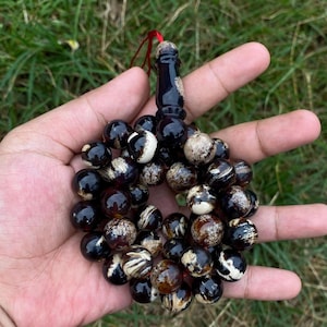 May include: A prayer bead rosary with dark brown and cream-colored beads. The beads are round and strung together with a dark brown decorative piece at the top. A red string is attached to the top.