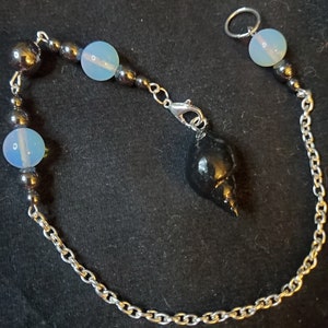 May include: A black shell pendulum with a silver chain and black and white beads. The chain has a silver clasp and a silver ring at the top.