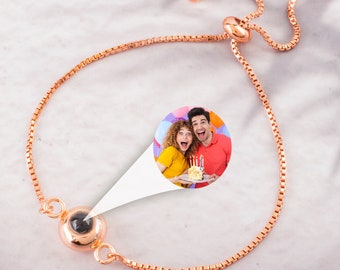 May include: A rose gold adjustable bracelet with a small round charm that reveals a photo when viewed from a specific angle. The photo shows a couple celebrating a birthday with a cake and balloons.