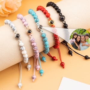 Puede incluir: Cinco pulseras de cuentas de colores con un peque&ntilde;o dije de plata en cada una. Los dijes tienen un dise&ntilde;o de ojo negro. Las pulseras est&aacute;n sobre una superficie blanca.