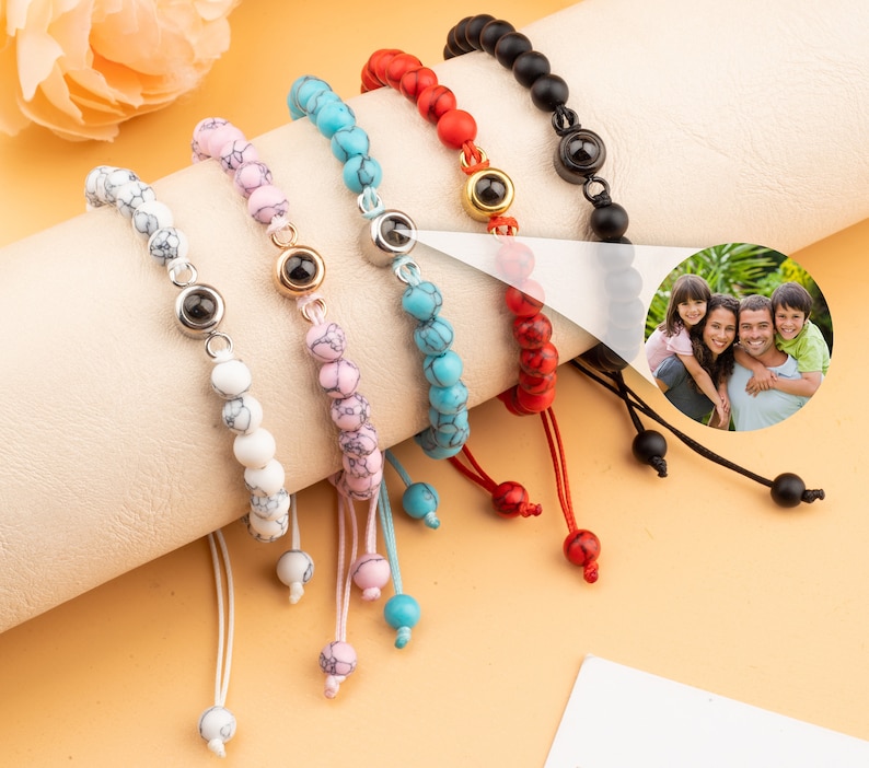 Puede incluir: Cinco pulseras de cuentas de colores con un peque&ntilde;o dije de plata en cada una. Los dijes tienen un dise&ntilde;o de ojo negro. Las pulseras est&aacute;n sobre una superficie blanca.