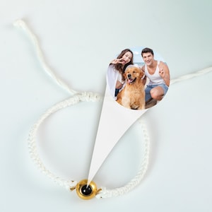 Puede incluir: Pulsera de cord&oacute;n blanco con un dije dorado que presenta una foto de una pareja y su perro. La foto muestra a un hombre y una mujer sonriendo y sosteniendo un golden retriever.