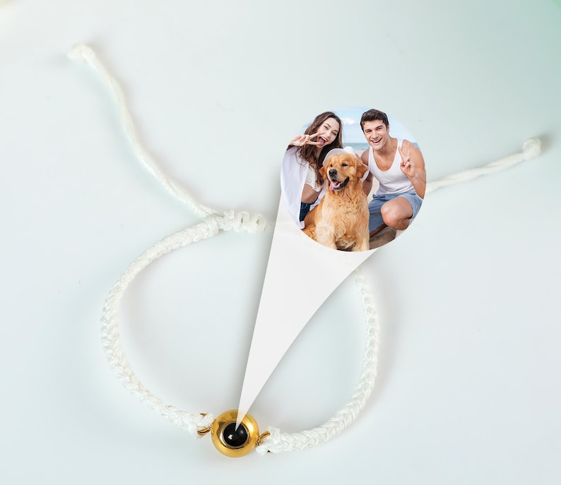Puede incluir: Pulsera de cord&oacute;n blanco con un dije dorado que presenta una foto de una pareja y su perro. La foto muestra a un hombre y una mujer sonriendo y sosteniendo un golden retriever.
