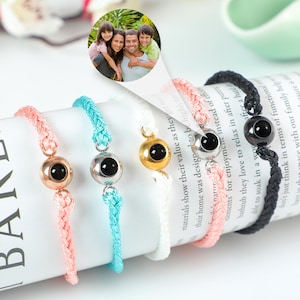 Puede incluir: Cinco pulseras trenzadas de colores vivos con un peque&ntilde;o dije redondo que contiene una foto en su interior. Los dijes son plateados, dorados, negros y dos tonos de azul diferentes.