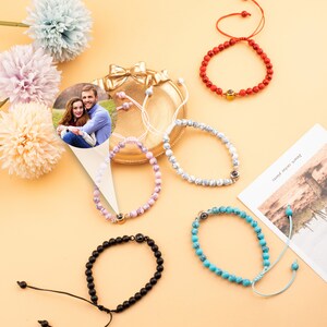 Puede incluir: Cinco pulseras de cuentas diferentes con un peque&ntilde;o dije de foto. Las pulseras son rojas, blancas, rosadas, negras y azules. El dije de foto es un peque&ntilde;o c&iacute;rculo con una foto de una pareja dentro.