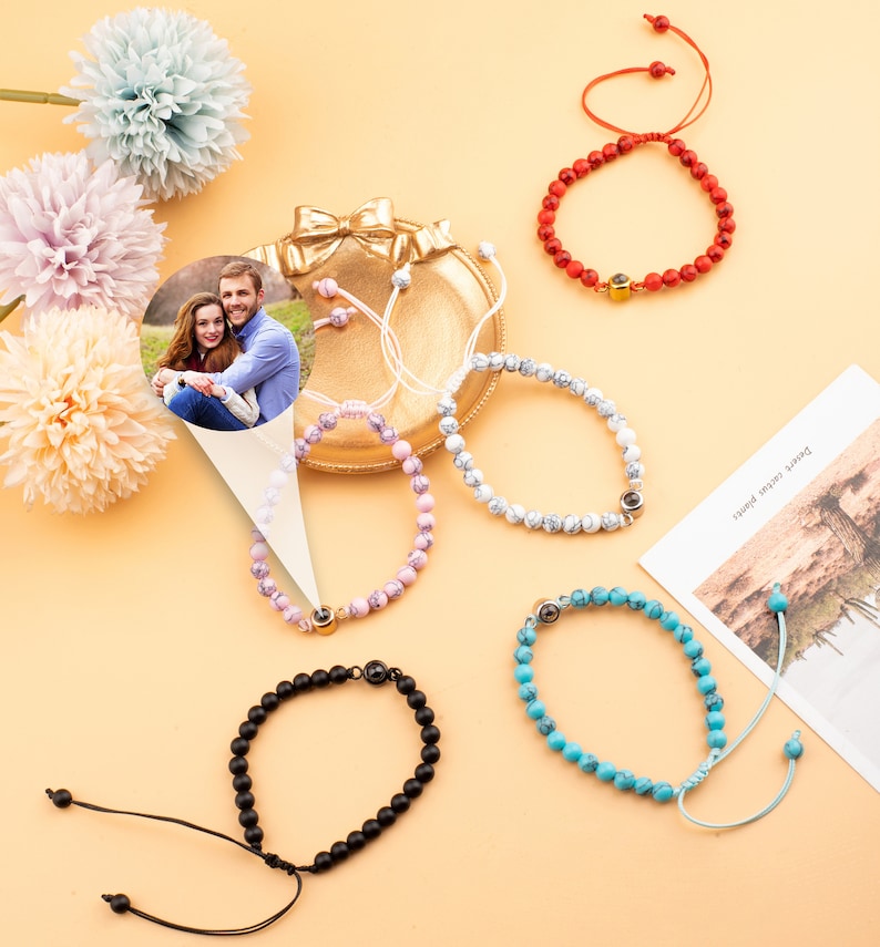 Puede incluir: Cinco pulseras de cuentas diferentes con un peque&ntilde;o dije de foto. Las pulseras son rojas, blancas, rosadas, negras y azules. El dije de foto es un peque&ntilde;o c&iacute;rculo con una foto de una pareja dentro.