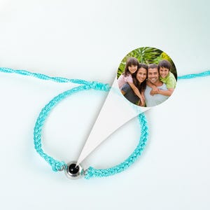 Puede incluir: Un brazalete trenzado turquesa con una cuenta de plata que contiene una foto negra. La foto muestra a una familia de cuatro personas sonriendo en un parque.