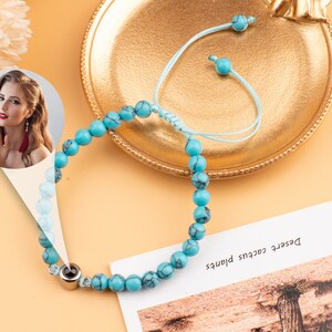 Puede incluir: Un brazalete de cuentas turquesa con un dije de plata. El brazalete est&aacute; en una bandeja dorada con una cuerda azul atada.