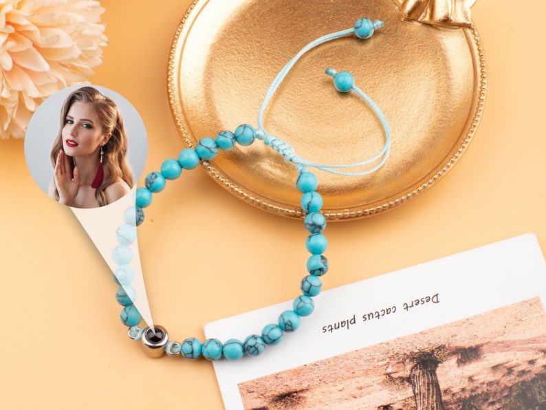 Puede incluir: Un brazalete de cuentas turquesa con un dije de plata. El brazalete est&aacute; en una bandeja dorada con una cuerda azul atada.